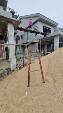 Perak, Malezya. 25 Ekim 2025: Bilinmeyen bir sanayi işçisi Permai İnşaat şantiyesindeki bitmemiş yüksek binalar arasındaki ahşap geçitten geçti.