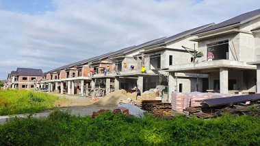 Perak, Malezya. 22 Kasım 2025: Beton makine mikseri üzerinde çalışan bir grup işçi, yük arabasında çimento taşıyıp, Permai Konut Projesi 'nin betonunu kaldırmak için metal kovayla halat makarasına döküyorlar.