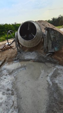 İnşaat alanındaki kum yığınının yanında eski bir çimento karıştırma makinesi..