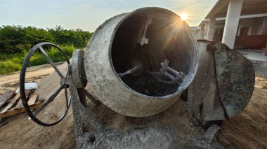 İnşaat alanındaki kum yığınının yanında eski bir çimento karıştırma makinesi..