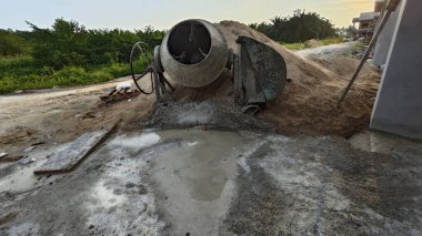 İnşaat alanındaki kum yığınının yanında eski bir çimento karıştırma makinesi..