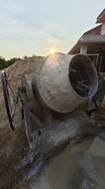 İnşaat alanındaki kum yığınının yanında eski bir çimento karıştırma makinesi..