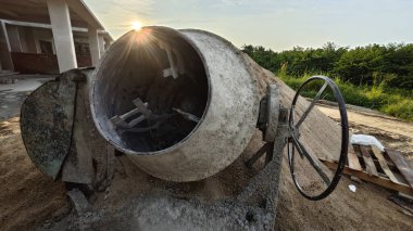 İnşaat alanındaki kum yığınının yanında eski bir çimento karıştırma makinesi..