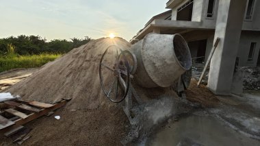 İnşaat alanındaki kum yığınının yanında eski bir çimento karıştırma makinesi..