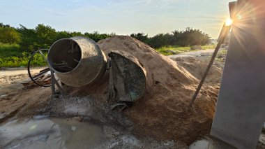 İnşaat alanındaki kum yığınının yanında eski bir çimento karıştırma makinesi..