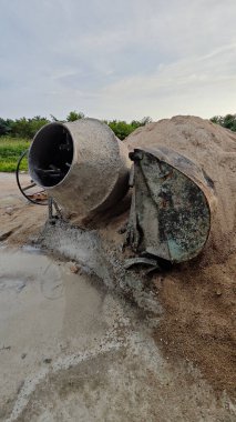 İnşaat alanındaki kum yığınının yanında eski bir çimento karıştırma makinesi..