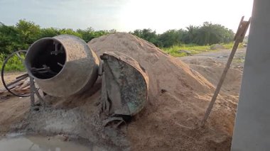 İnşaat alanındaki kum yığınının yanında eski bir çimento karıştırma makinesi..