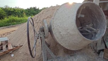 İnşaat alanındaki kum yığınının yanında eski bir çimento karıştırma makinesi..