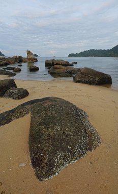 Kumlu sahil kenarında bulunan kayalık kayalara doğru bakıyor..