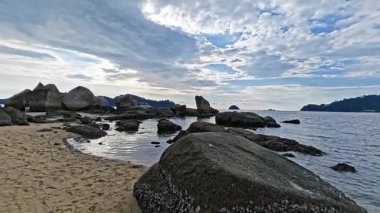 Perak, Malezya. 30 Aralık 2025: Bilinmeyen bir kadın Pangkor Adası 'nın kumlu sahil kıyısındaki kayalık kayanın etrafında duruyor.