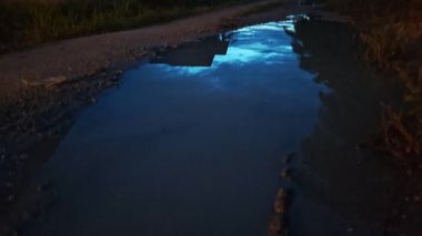 İzole edilmiş toprak yolun gece manzarası. Yakınlardaki sokak lambası alanına doğru gölet çukurları var..