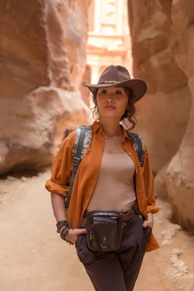 峡谷的底部站着一个漂亮的姑娘，她背着背包，头戴牛仔帽，身穿橙色衬衫，向前看 — 图库照片