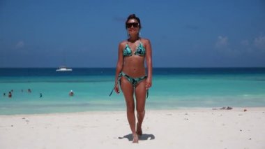 A beautiful girl in a blue swimsuit walks from the sea against the background of yachts, sexually wagging her ass