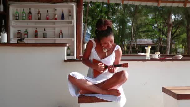 Mignonne fille s'assoit sur un tabouret jambes croisées et joue de la guitare — Video