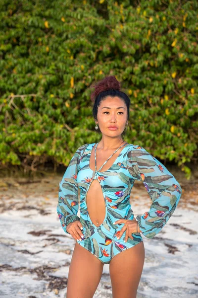 Beautiful sexy brunette girl in a bikini with a print of exotic flowers and birds stands on the beach against the mangrove