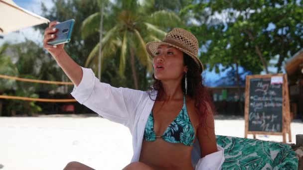 Piękna Dziewczyna Bikini Kapeluszu Siedzi Plaży Uśmiechnięta Robi Sobie Selfie — Wideo stockowe