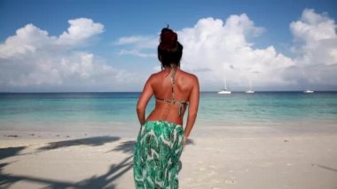 Mavi mayo giymiş güzel ve narin bir kız denizin arka planında ve yatlarda dans ediyor, kalçalarını sallıyor.