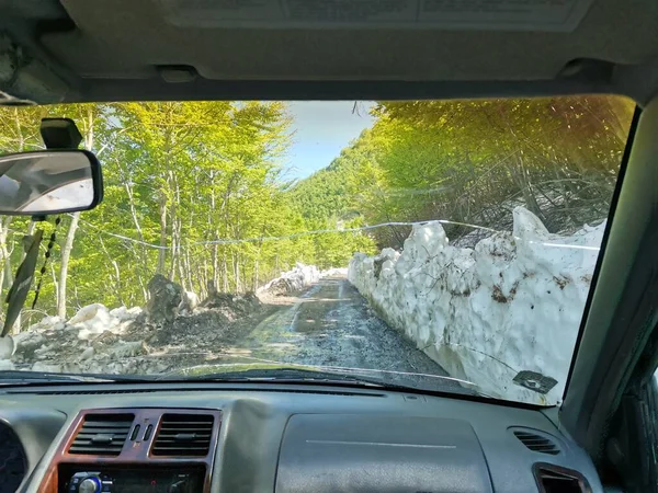 Dirt road gravel road with snow walls in spring in the albanian mountains front window view, christian driver