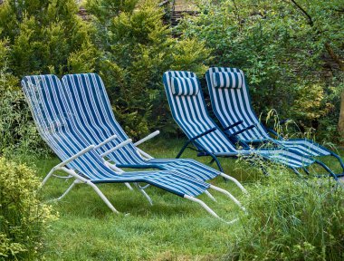 Bahçenin arka bahçesinin bir kısmı yeşil çimenlikli ve dinlenmek için çizgili güneş pansiyonlu.