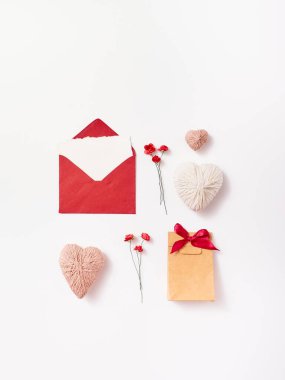 Beyaz arkaplandaki tebrik kartı için el yapımı zarf, hediye, kalp, gül ve tüy içeren düz kartpostal kompozisyonu
