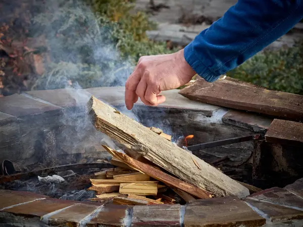 Taşların yanında şenlik ateşi yakarken tahta kütüğe dokunan adam.