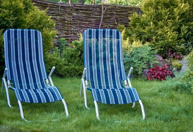 Bahçenin arka bahçesinin bir kısmı yeşil çimenlikli ve dinlenmek için çizgili güneş pansiyonlu.