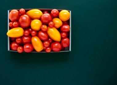 Karton bir kutuda kırmızı ve sarı domatesler. Fotokopi alanı olan koyu bir zemin üzerinde.
