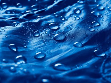 Su geçirmez zar kumaşına su damlıyor. Mavi su geçirmez kumaşın dokusunun detaylı görünümü.