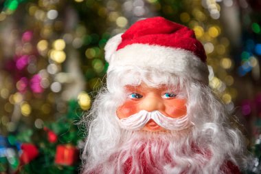 Oyuncak Noel Baba 'nın portresi, parlak Noel çelenklerinin bulanık arka planında.