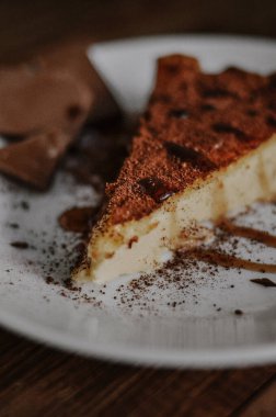 Lezzetli bir dilim kahveli cheesecake kakaoyla kaplı beyaz tabakta çikolata ve koyu ahşap arka planda karamel.