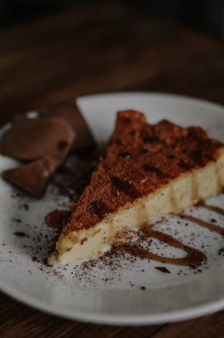Lezzetli bir dilim kahveli cheesecake kakaoyla kaplı beyaz tabakta çikolata ve koyu ahşap arka planda karamel.