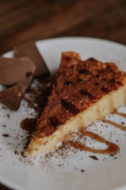Lezzetli bir dilim kahveli cheesecake kakaoyla kaplı beyaz tabakta çikolata ve koyu ahşap arka planda karamel.