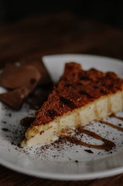 Lezzetli bir dilim kahveli cheesecake kakaoyla kaplı beyaz tabakta çikolata ve koyu ahşap arka planda karamel.