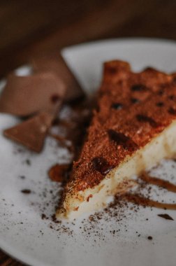 Lezzetli bir dilim kahveli cheesecake kakaoyla kaplı beyaz tabakta çikolata ve koyu ahşap arka planda karamel.
