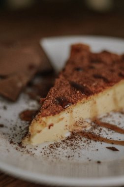Lezzetli bir dilim kahveli cheesecake kakaoyla kaplı beyaz tabakta çikolata ve koyu ahşap arka planda karamel.