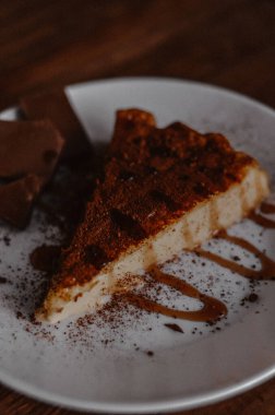 Lezzetli bir dilim kahveli cheesecake kakaoyla kaplı beyaz tabakta karamel ve çikolatalı koyu ahşap arka planda yakın plan