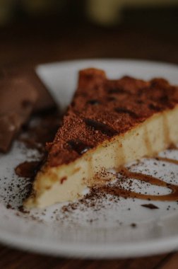 Lezzetli bir dilim kahveli cheesecake kakaoyla kaplı beyaz tabakta çikolata ve koyu ahşap arka planda karamel.