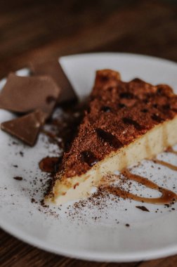 Lezzetli bir dilim kahveli cheesecake kakaoyla kaplı beyaz tabakta çikolata ve koyu ahşap arka planda karamel.
