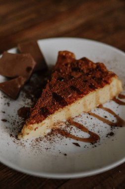Lezzetli bir dilim kahveli cheesecake kakaoyla kaplı beyaz tabakta karamel ve çikolatalı koyu ahşap arka planda yakın plan