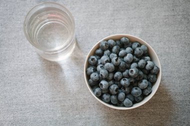 Tabak dolusu taze yaban mersini ve bir bardak su, düzlük. Sağlıklı tatlı olarak bir sürü böğürtlen. Yaz meyveleri masada. Doğal vitamin kaynağı, sağlıklı beslenme.