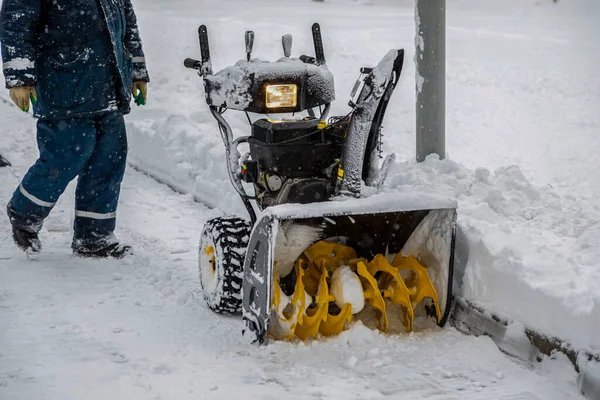 Snowblower estacionado no parque durante uma queda de neve. A pessoa vai a um limpa-neves. — Fotografia de Stock