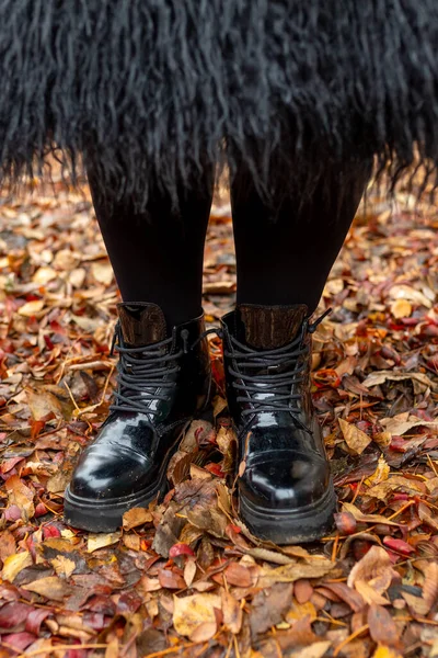 Thick female legs in comfortable black boots on autumn leaves. Stability, strength, confidence concept.