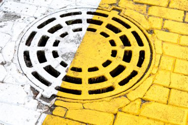 Sarı ve beyaz yol işaretlerinin altında kapalı lağım çukuru var. Yakın plan.