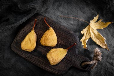 Ahşap bir mutfak tahtasındaki üç kuru armut ve düşmüş bir akçaağaç yaprağının durgun yaşamı. Sağlıklı yeme kavramı