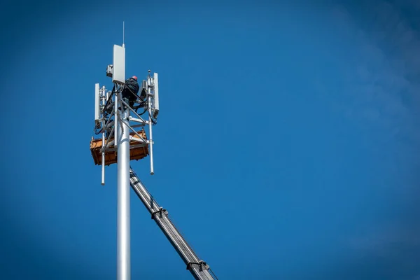 İşçiler, mavi gökyüzünün arka planındaki baz istasyonuna 3G, 4G, 5G, 5G ve antenli hücresel baz istasyonu kurarlar. Mobil telekomünikasyon ekipmanları. Boşluğu kopyala