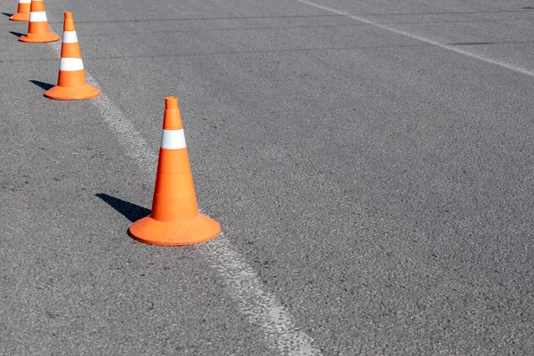 Bright orange traffic cones on asphalt road. Traffic signal cones considered universal products, with their help you can quickly and easily ensure safety of all road.