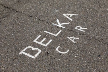 Araba paylaşım şirketi BELKA 'nın asfalttaki şirket yazıtları arabanın park yerini gösteriyor. Belka arabası Rus şehirlerinde araba paylaşım hizmetleri sunmaktadır. Araba kiralama işlemleri mobil uygulama üzerinden yapılabilir. İllüstrasyon Editörü.