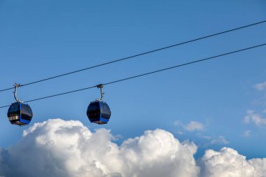 Bulutların üzerinde gökyüzüne karşı iki mavi teleferik. Teleferikle turist gezisi.