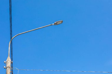 Sokak lambası ve mavi gökyüzüne bağlı kabloları olan beton elektrik direği. Boşluğu kopyala