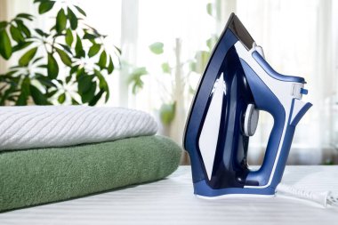 Ev ödevi konsepti: içeride ütü masasında yeşil kıyafetler ütü ve havlular. Evde etkinlikler ütü ve havlu katlama